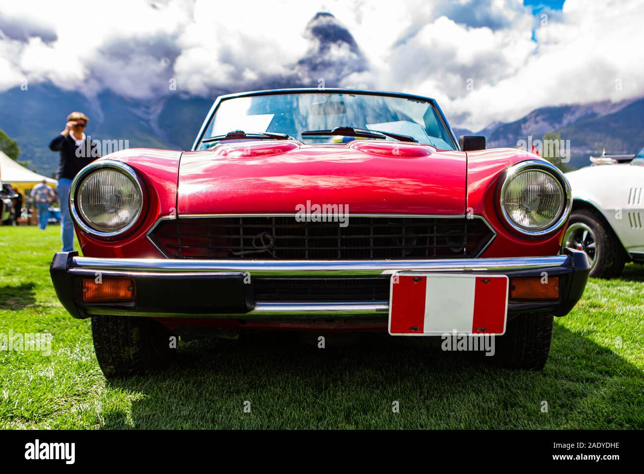 classic old American red car front low angle view, headlights light lamps and a black grille with chrome bumper, during outdoor antique cars show Stock Photo