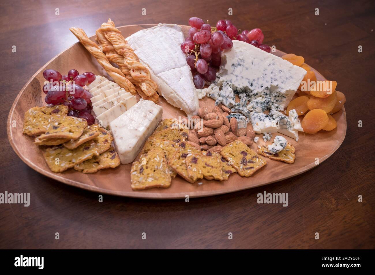 Wooden cheese platter with brie, assorted cheeses, red grapes, crackers