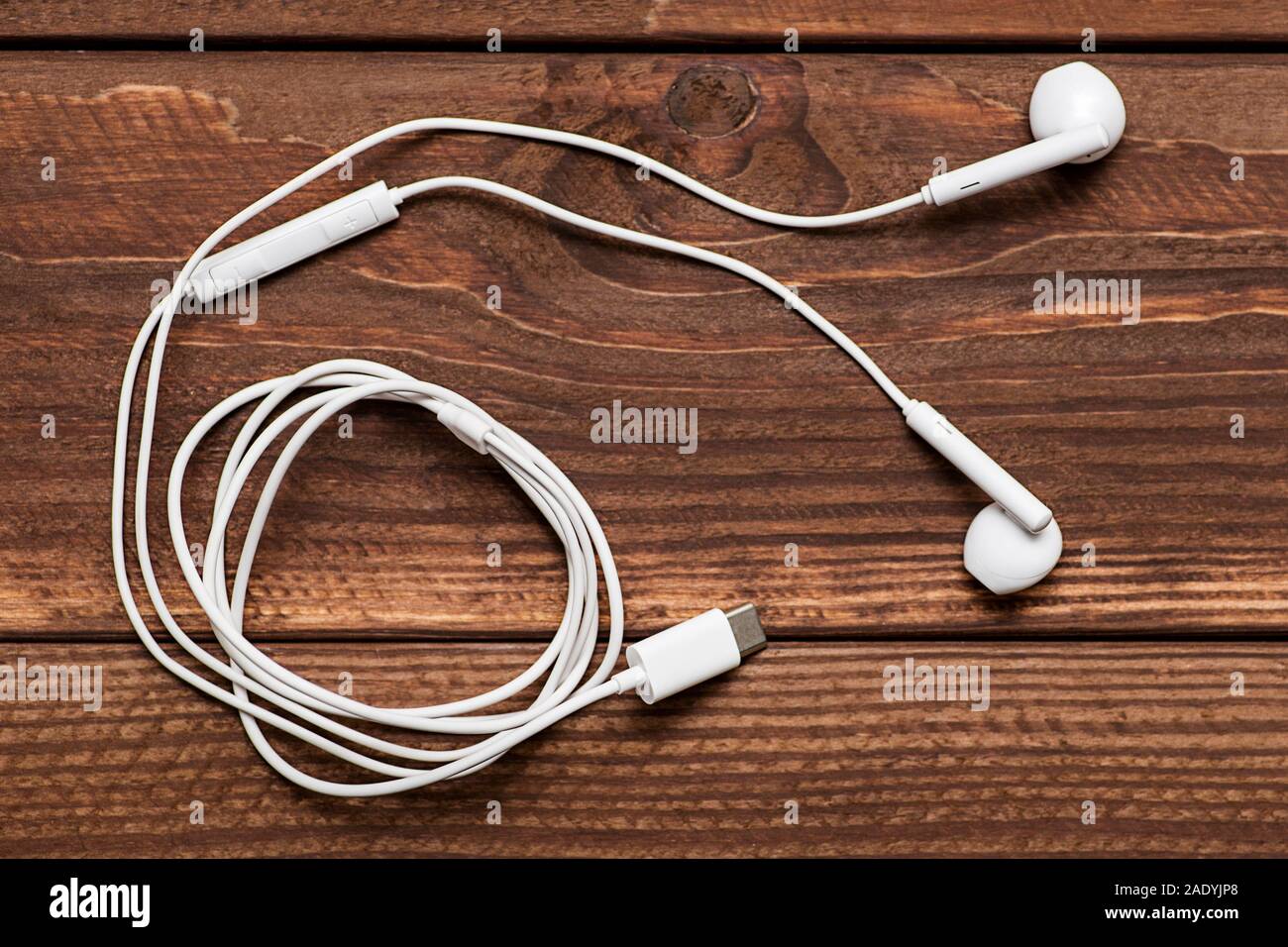 Modern white earphone, white in ear headphone on wooden table. White earphones over wooden board. Stock Photo