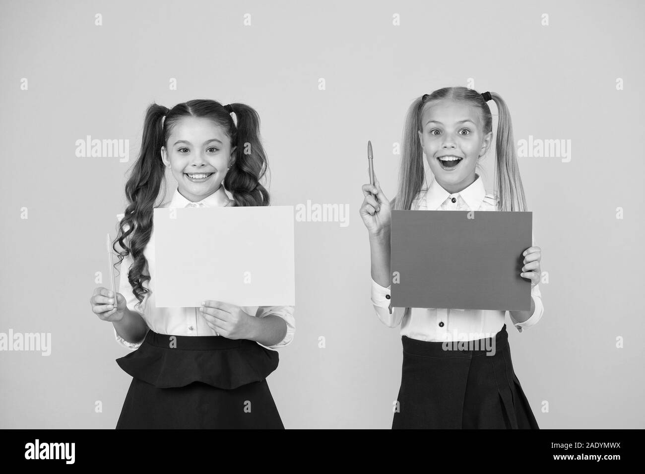 Got idea. Small cute kids smiling of genius idea. Happy girls holding paper sheets for writing idea on yellow background. Little children with empty paper for creative idea, copy space. Stock Photo