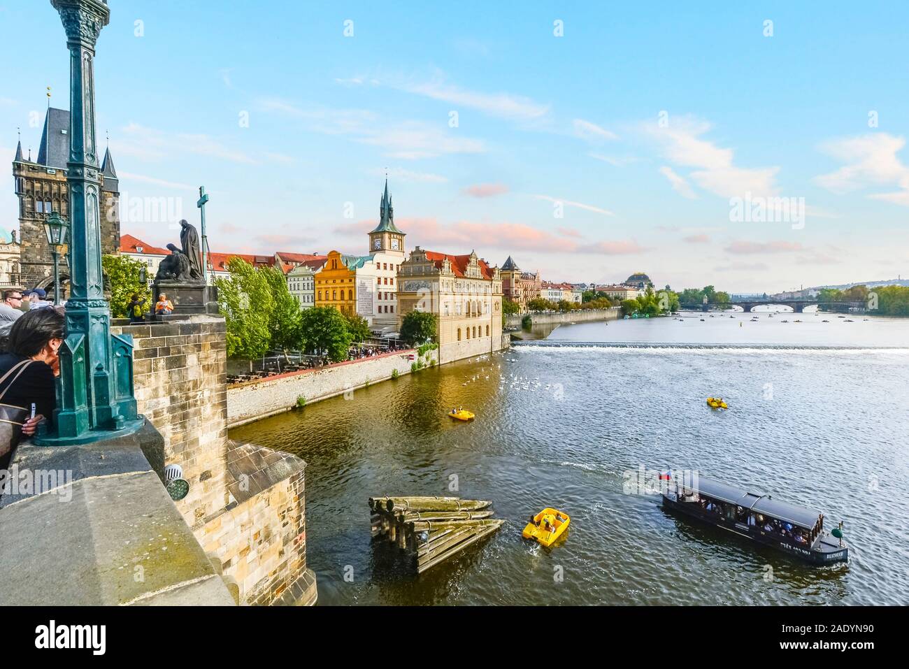 A young woman relaxes on the Charles Bridge as pedal and tourist boats cruise alongside the swans in the Vltava River in Prague, Czechia. Stock Photo