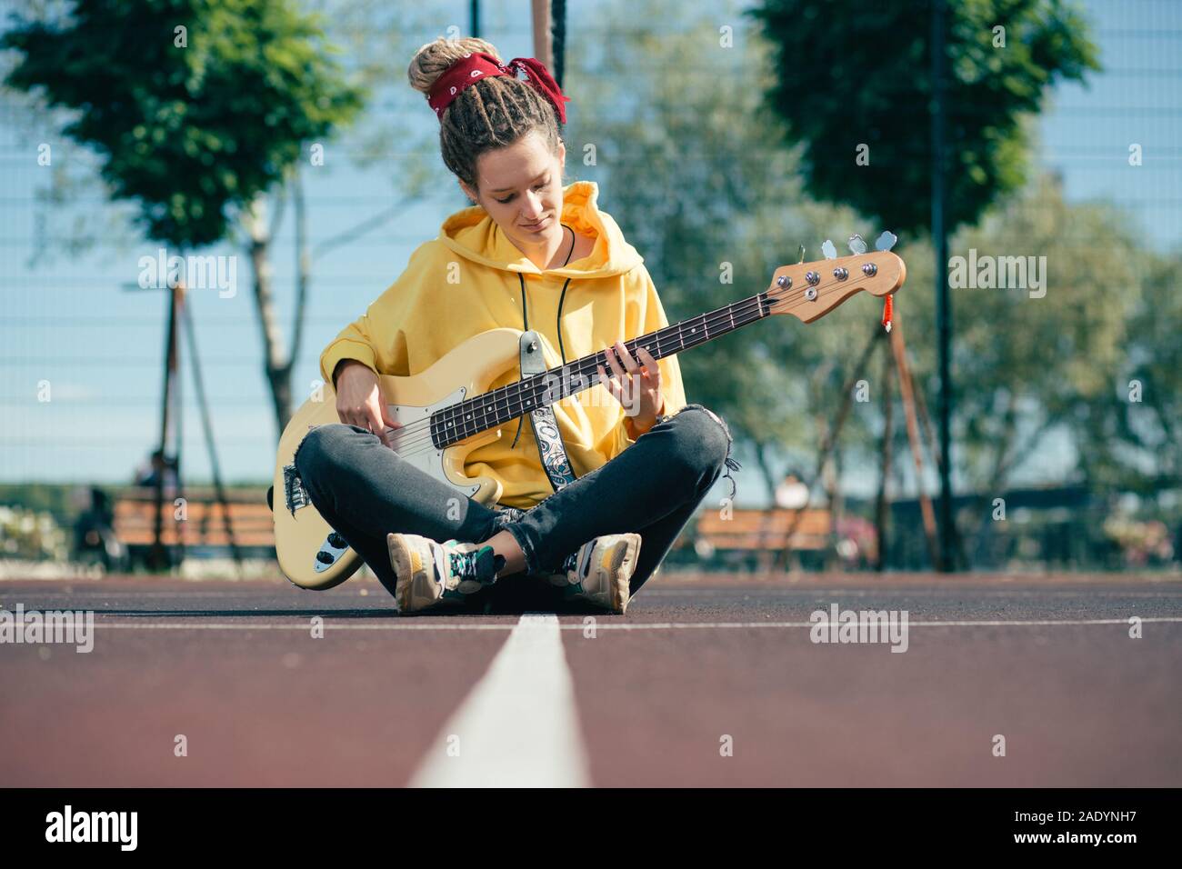 Calm musician playing the guitar while sitting alone at the sports ground Stock Photo