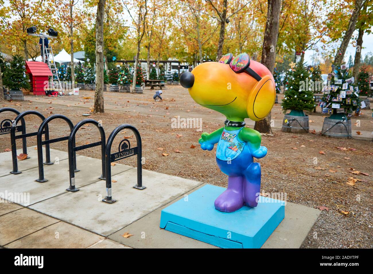 A rainbow-colored statue of Snoopy comic character near bike stands and decorated Christmas trees at Windsor Town Green, in California. Stock Photo