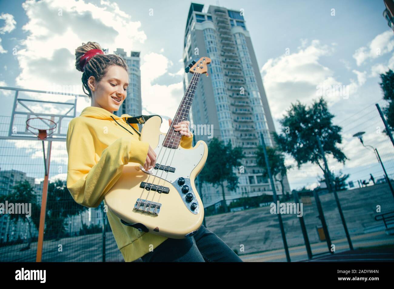 Waist up of young lady with dreadlocks playing the guitar outdoors Stock Photo