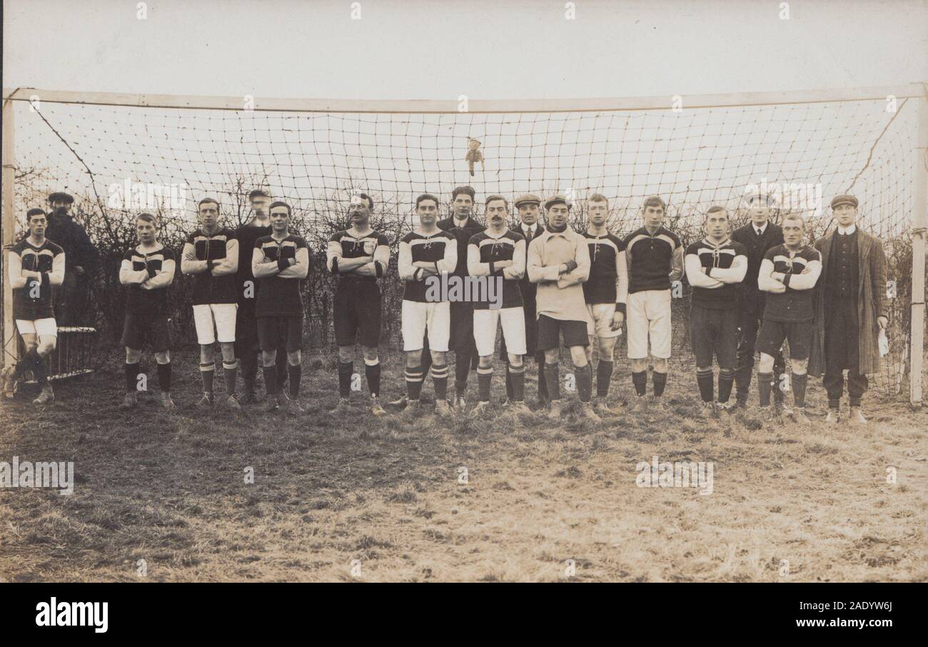 Vintage Early 20th Century Photographic Postcard Showing a Grass Roots Football Team Posing Between The Posts of a Goal. Mascot Hanging in The Goal Net Stock Photo