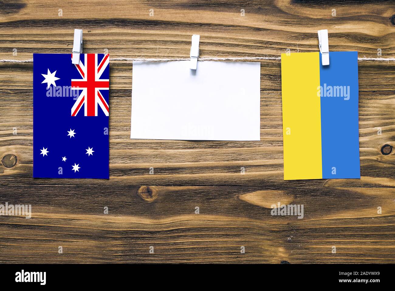 Hanging flags of Australia and Ukraine attached to rope with clothes pins with copy space on white note paper on wooden background.Diplomatic relation Stock Photo