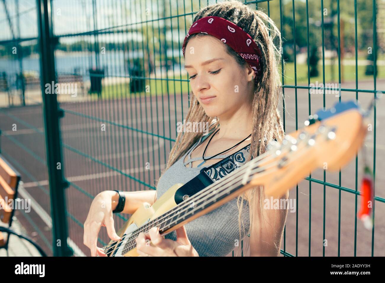 Peaceful musician leaning on the chain link fence and playing the guitar Stock Photo