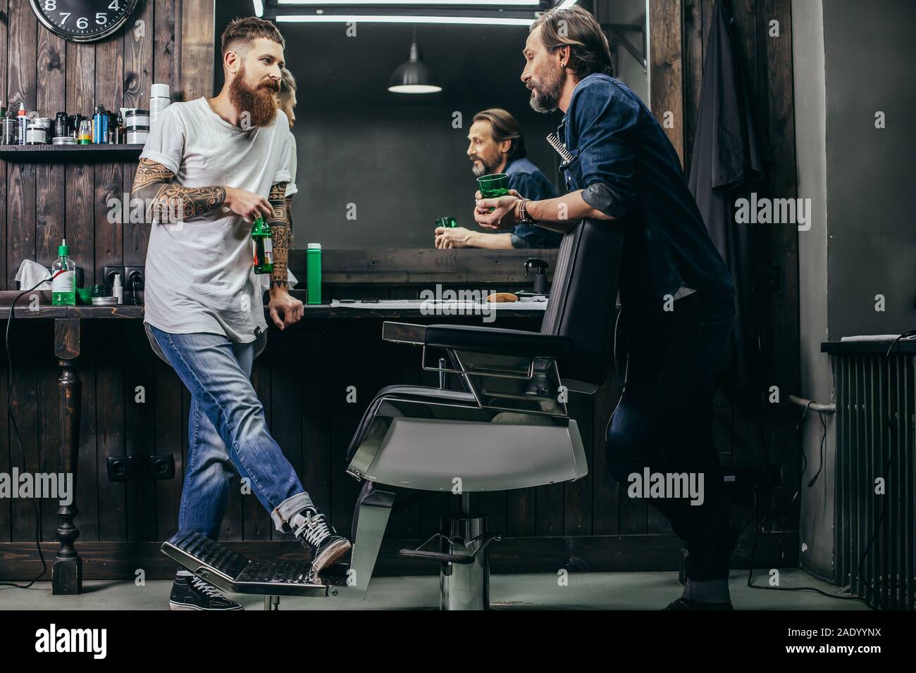 Two bearded men drinking beer while talking in barbershop Stock Photo