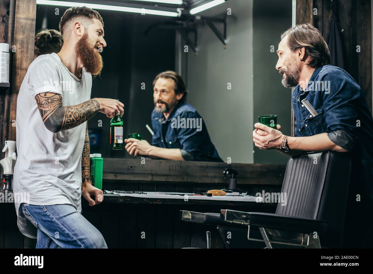 Two men smiling while drinking beer in barbershop Stock Photo