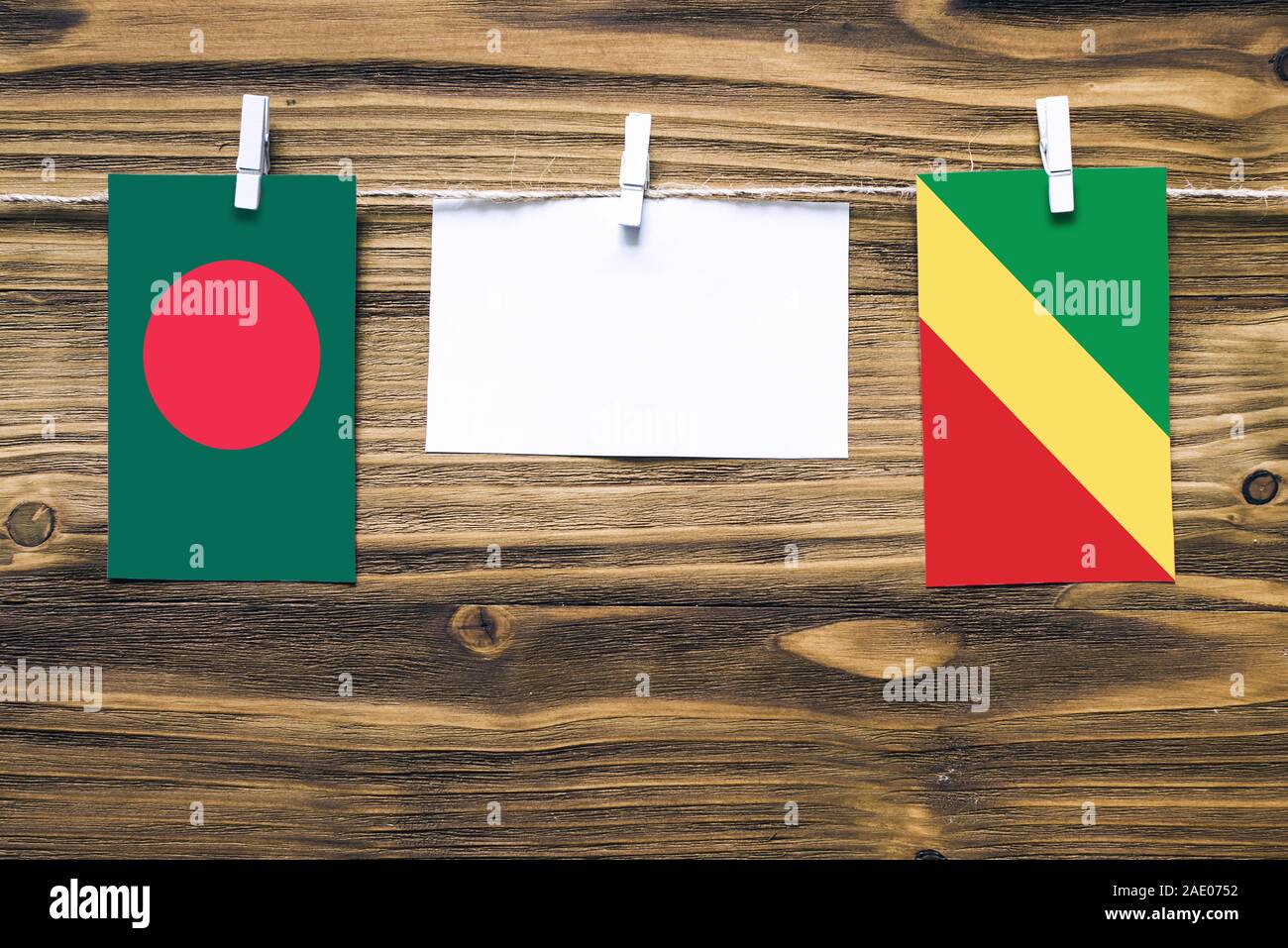Hanging flags of Bangladesh and Republic Of The Congo attached to rope with clothes pins with copy space on white note paper on wooden background.Dipl Stock Photo