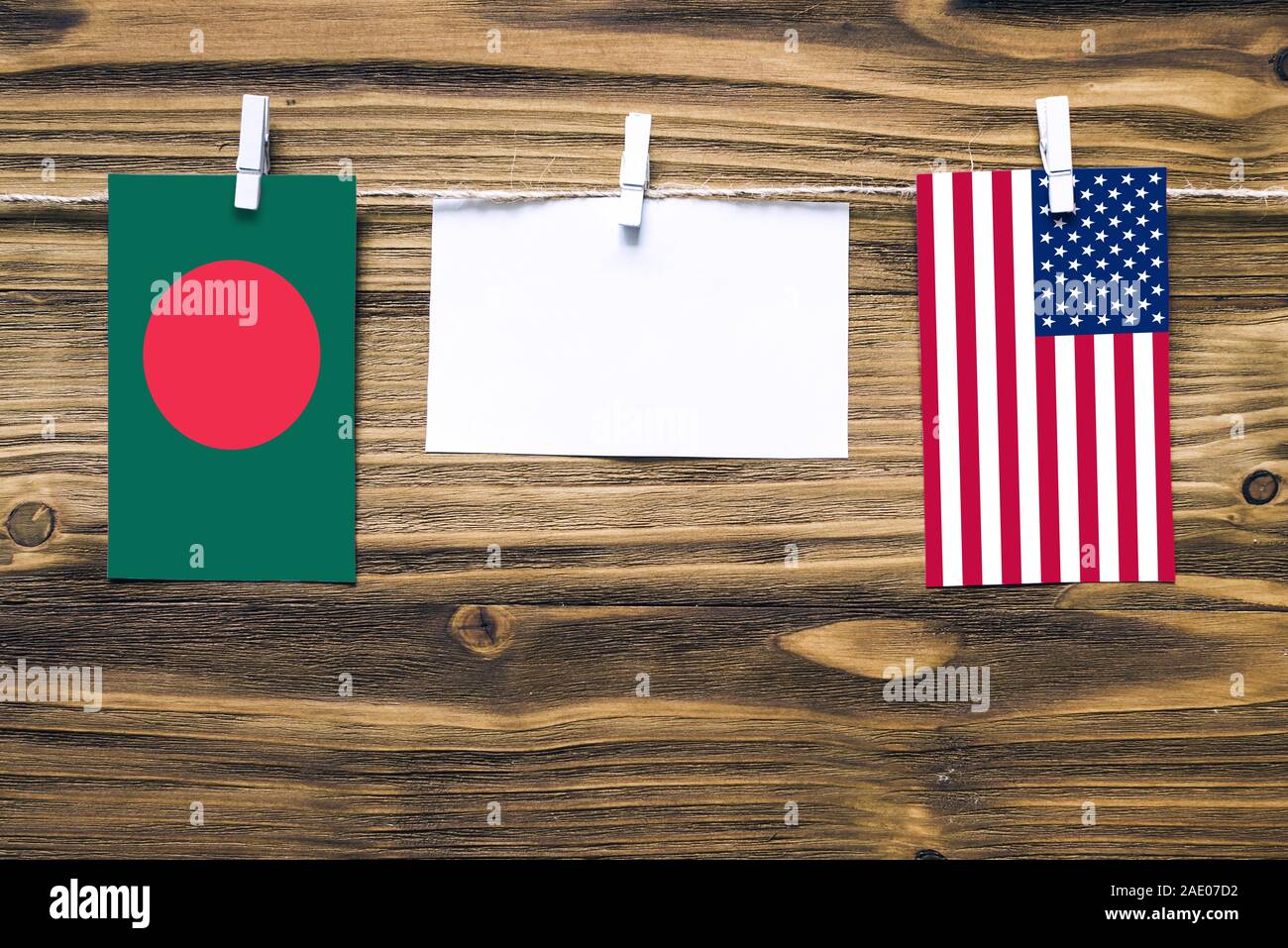 Hanging flags of Bangladesh and United States attached to rope with clothes pins with copy space on white note paper on wooden background.Diplomatic r Stock Photo