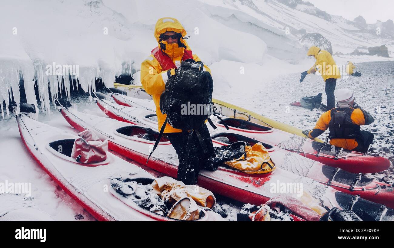 Extreme weather conditions in Antarctica as snow falls on sea kayaks, men and gear on an icy beach on the Antarctic peninsula. Brown Bluff, Antarctica Stock Photo