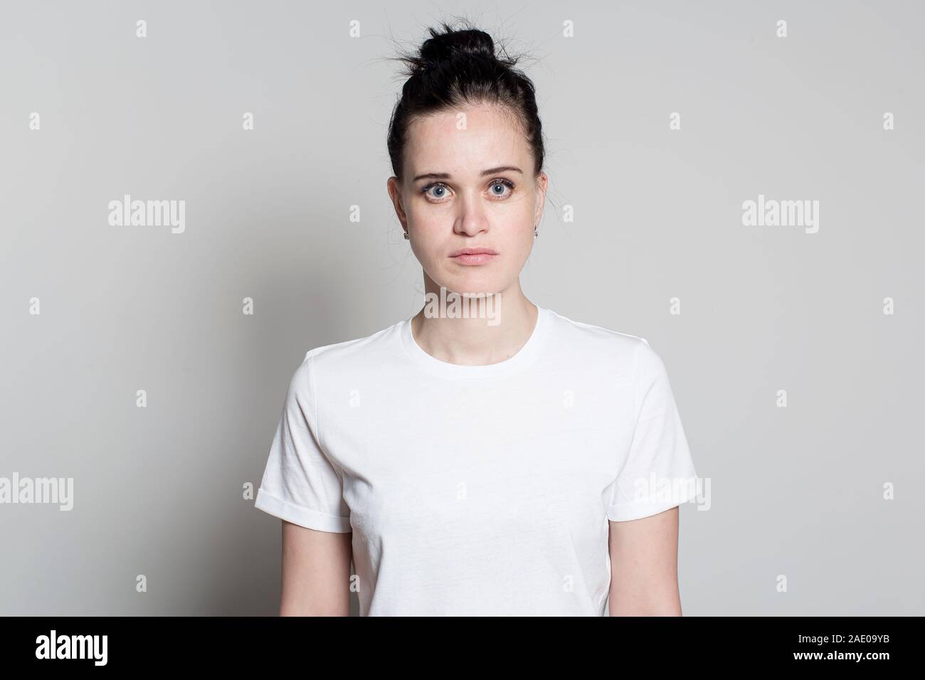 Little frightened, unsure of herself, a pretty young woman stares intently into the camera with big eyes. Stock Photo
