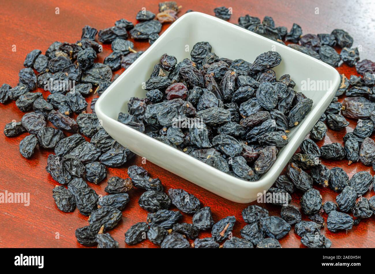 Black raisins in a bowl and on a wooden table. Stock Photo