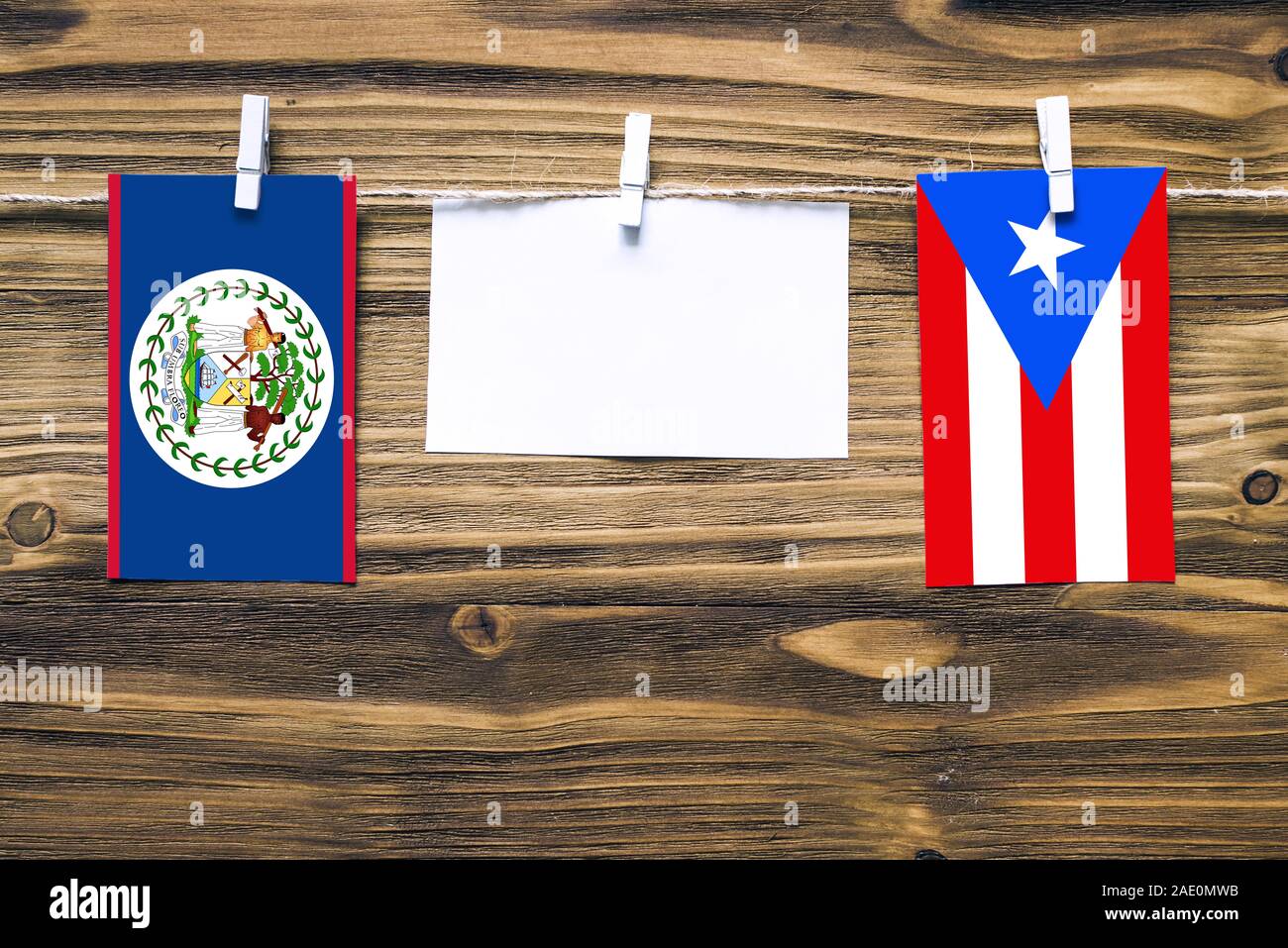 Hanging flags of Belize and Puerto Rico attached to rope with clothes pins with copy space on white note paper on wooden background.Diplomatic relatio Stock Photo