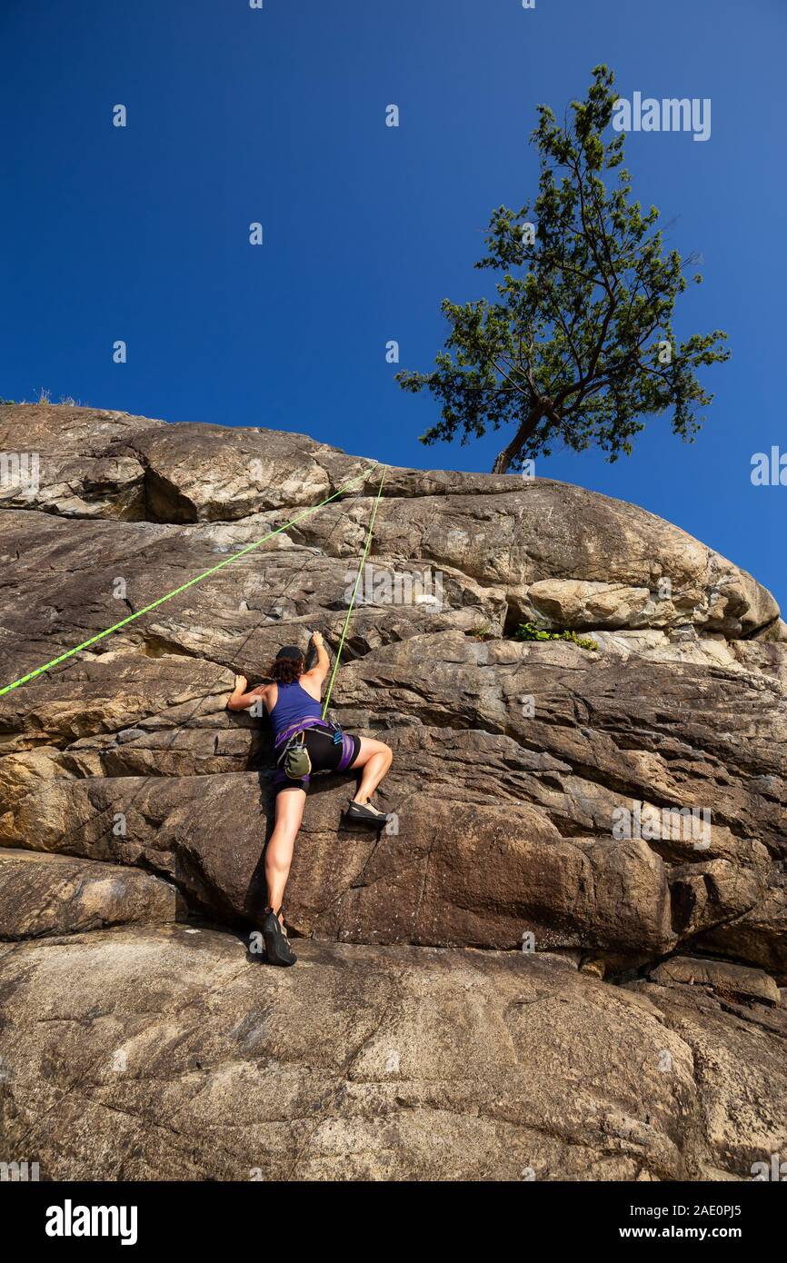 Adventurous Girl is Rock Climbing up a Steep Cliff during a summer sunset. Taken in Lighthouse