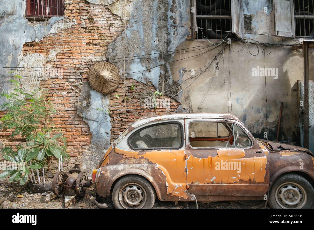 Bangkok,Thailand. November 30,2019 : Abandoned wrecked orange vintage car against old brick wall background. Stock Photo