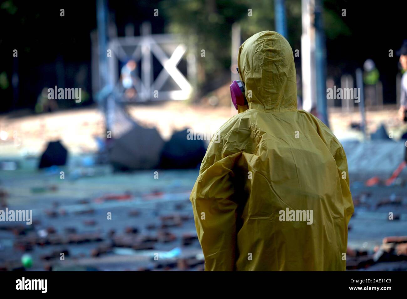 A protestor wearing a yellow rain jacket and tear gas mask examines the scene at Polytechnic, with the ground dyed blue and littered with bricks. Stock Photo