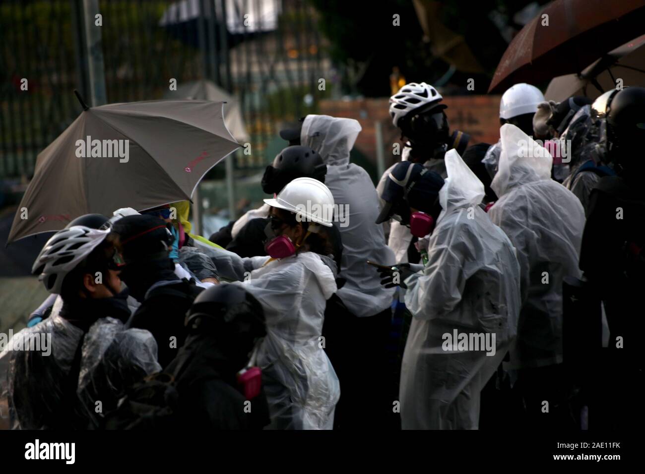 Protestors don rain jackets and tear gas masks to face off with police while using umbrellas as defensive shields against surveillance and attacks. Stock Photo