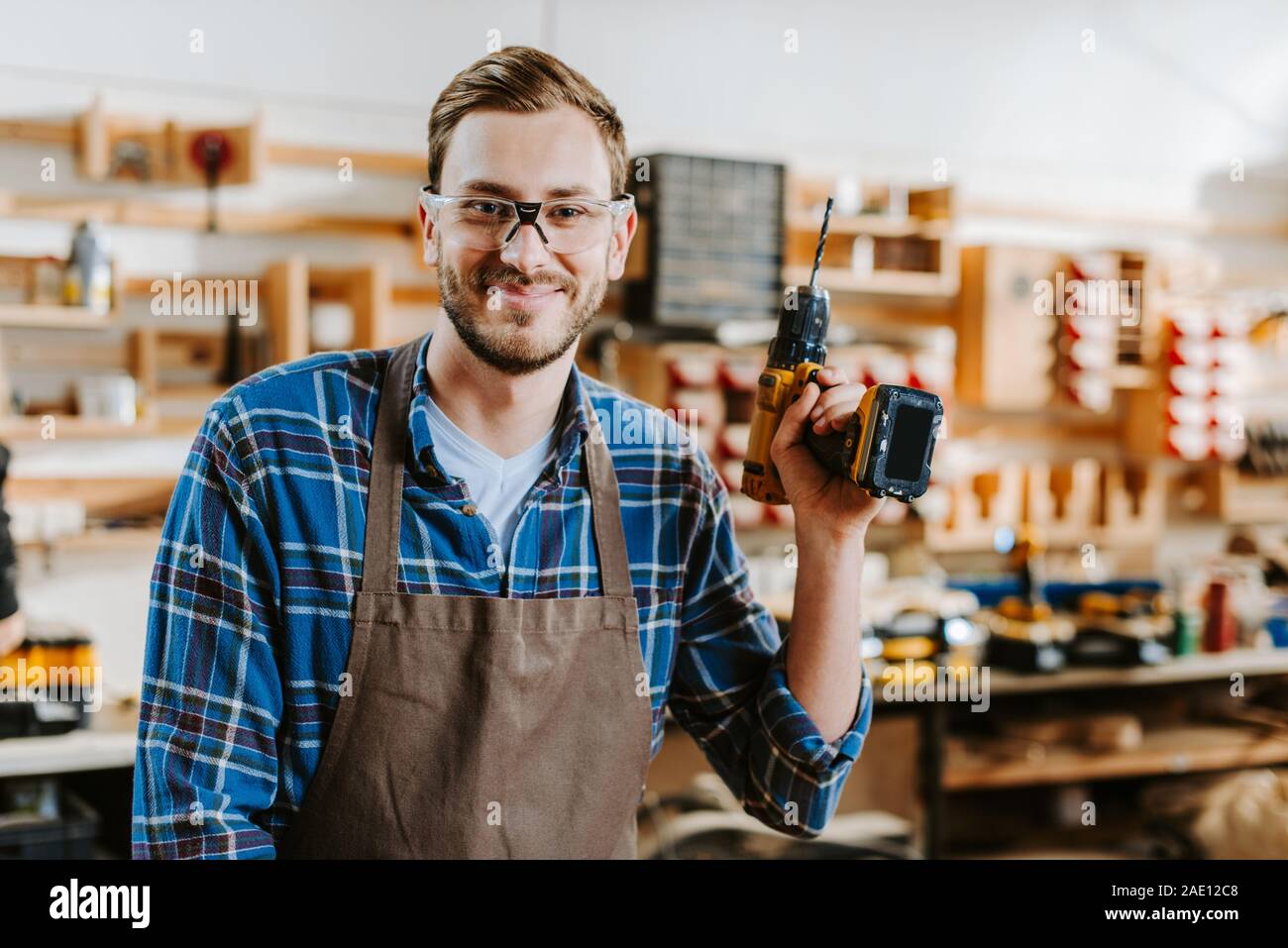 happy carpenter in goggles and apron holding hammer drill Stock Photo