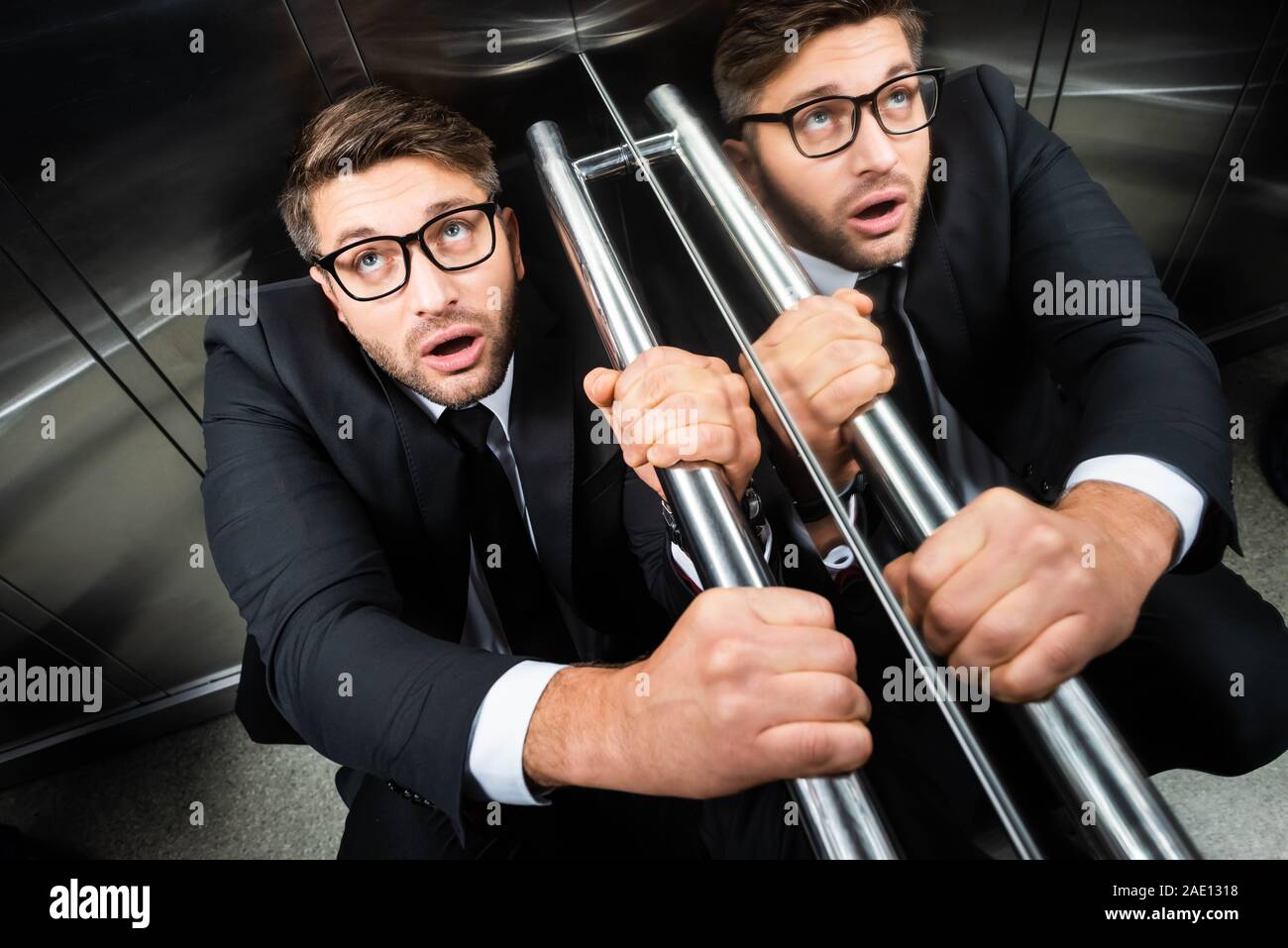 high angle view of scared businessman in suit with claustrophobia sitting on floor in elevator Stock Photo