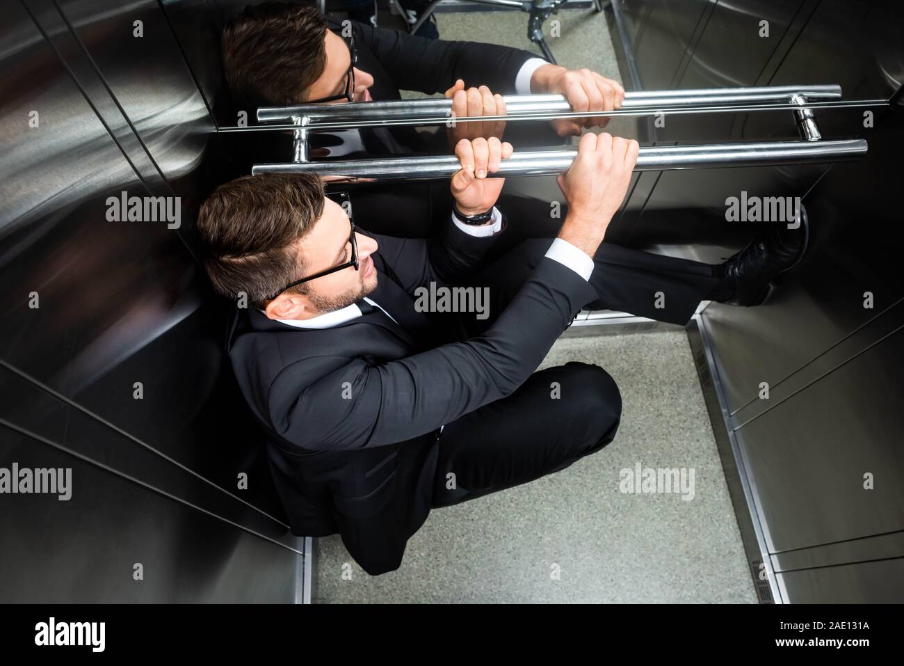 high angle view of scared businessman in suit with claustrophobia sitting on floor in elevator Stock Photo