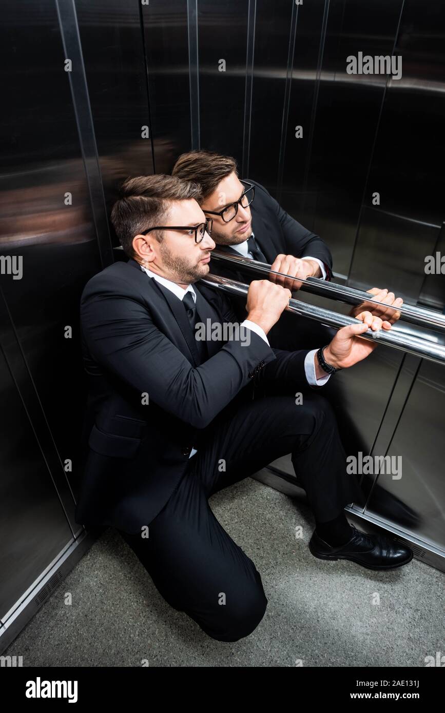 high angle view of scared businessman in suit with claustrophobia sitting on floor in elevator Stock Photo