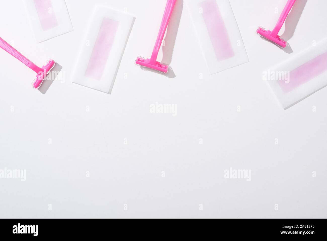 top view of pink razors and depilation wax stripes on white background