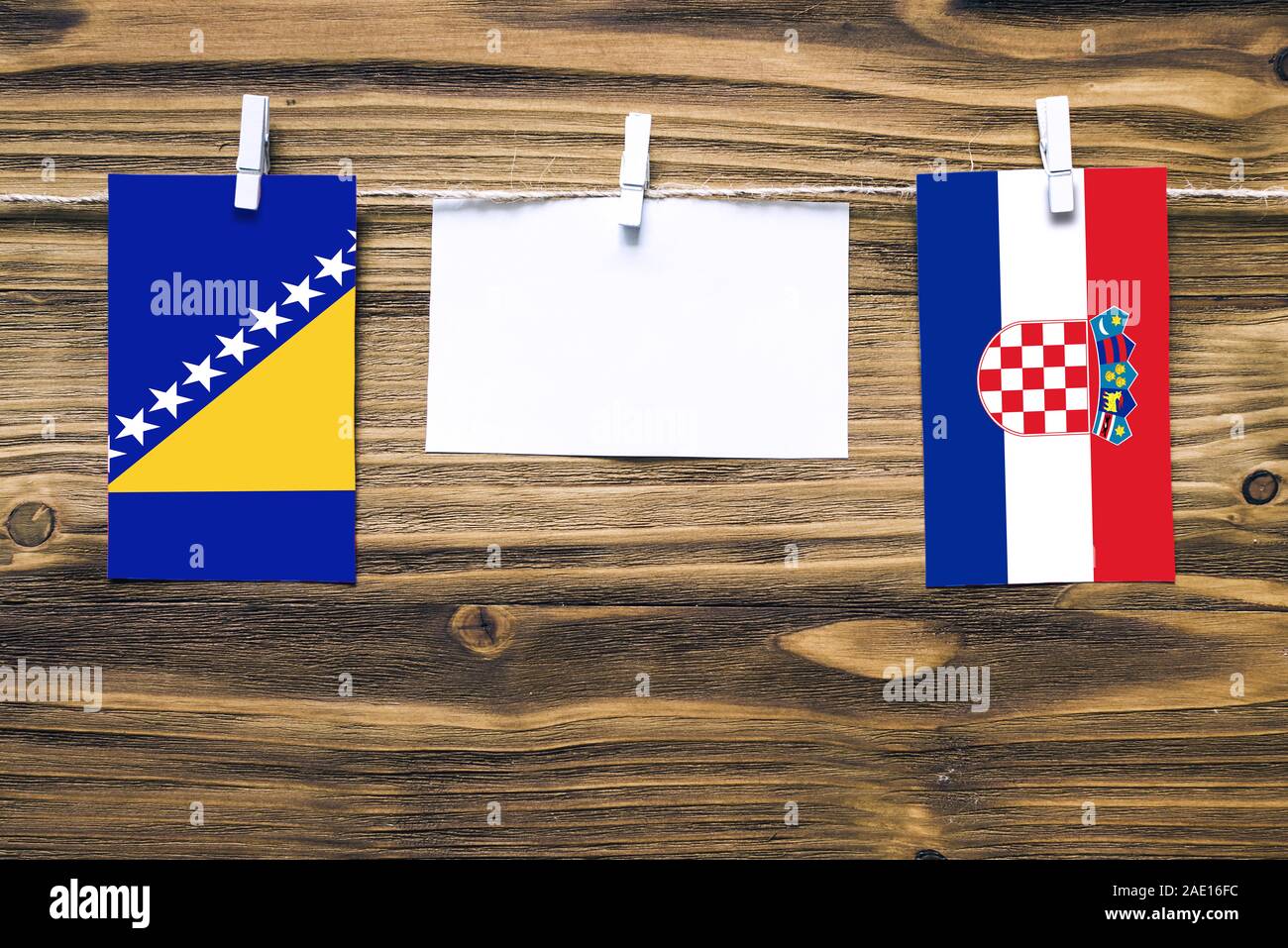Hanging flags of Bosnia Herzegovina and Croatia attached to rope with clothes pins with copy space on white note paper on wooden background.Diplomatic Stock Photo