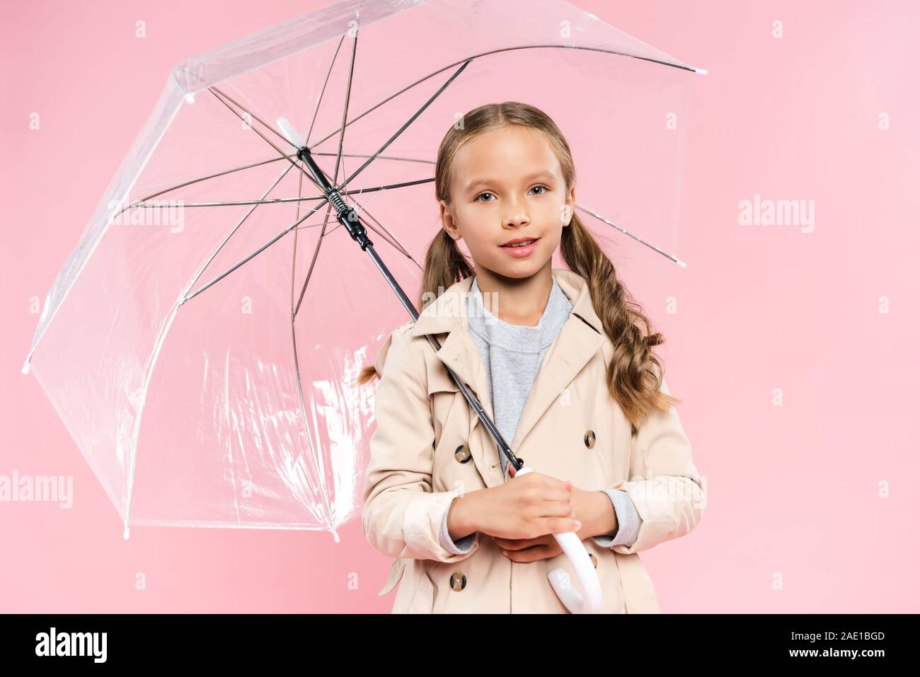 smiling kid in autumn outfit holding umbrella isolated on pink Stock Photo
