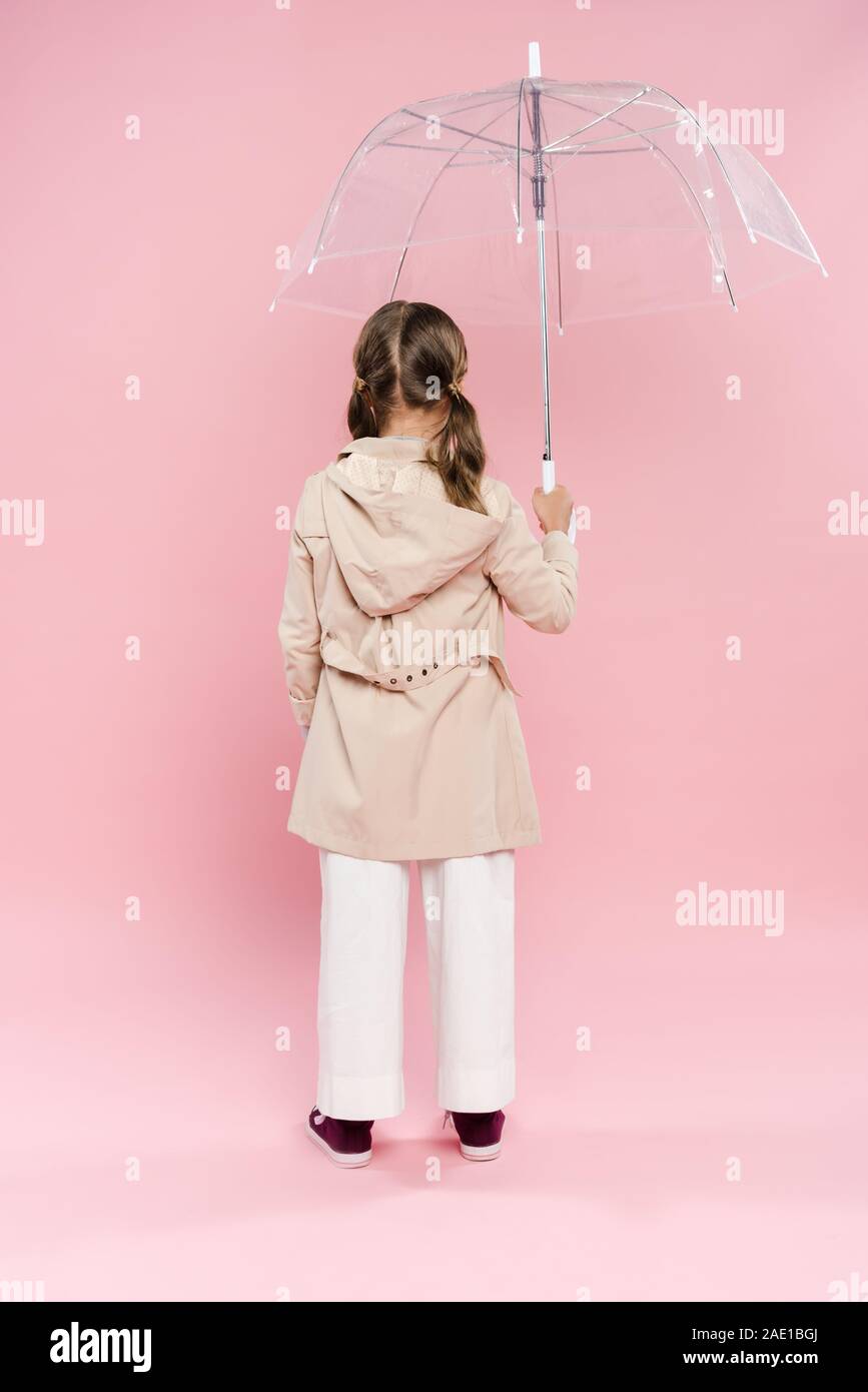 back view of kid in autumn outfit holding umbrella on pink background Stock Photo