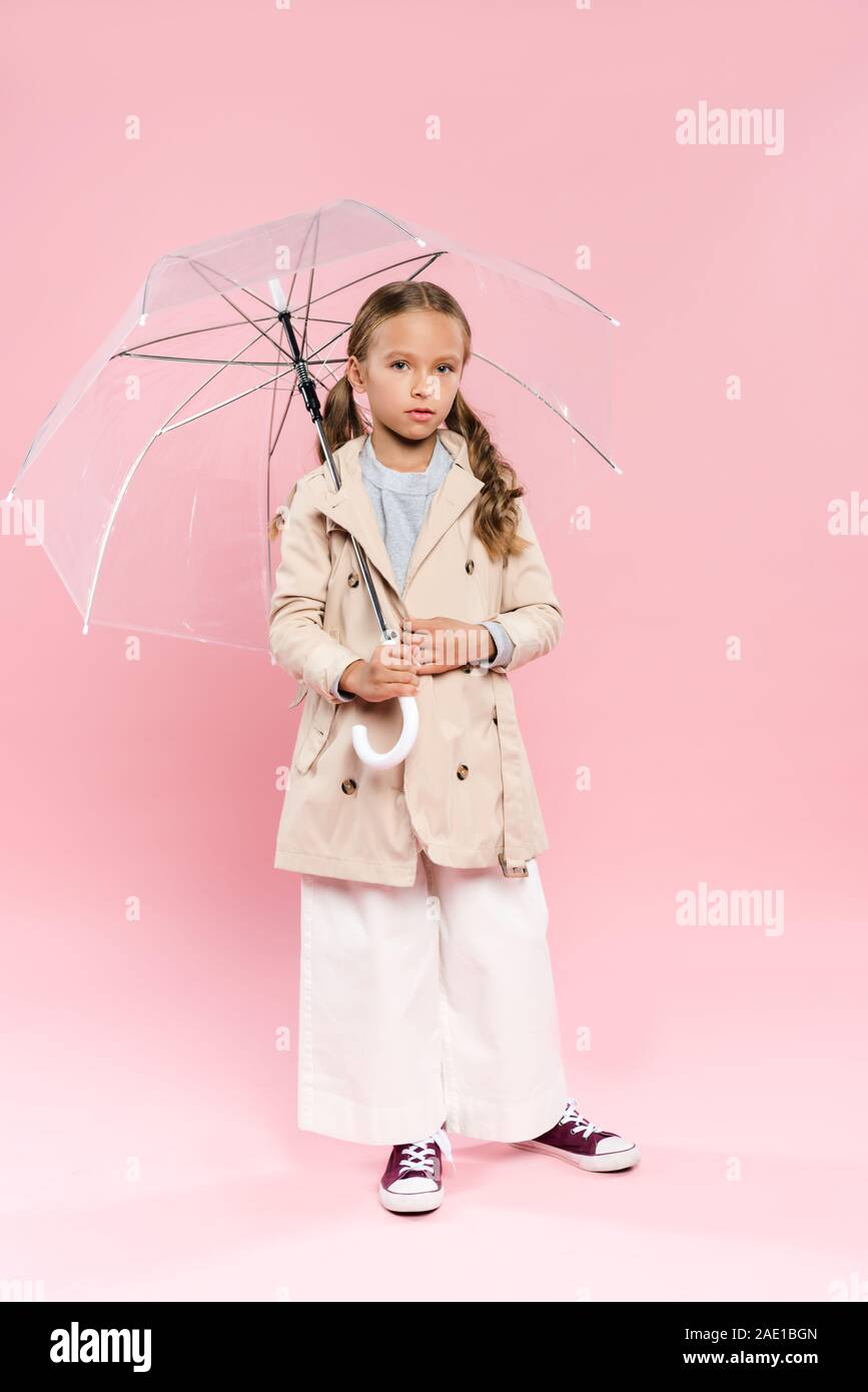 kid in autumn outfit holding umbrella on pink background Stock Photo