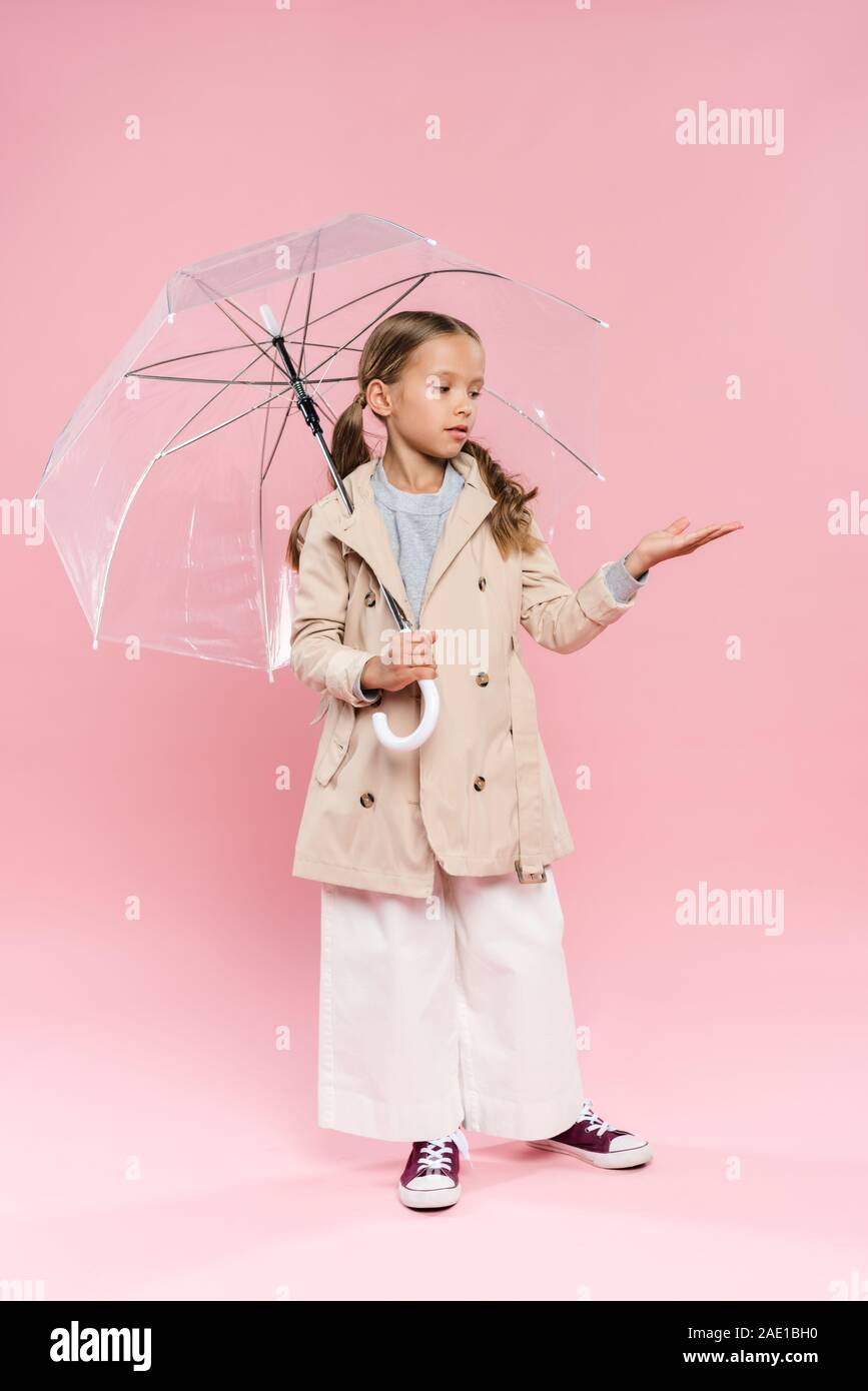 kid in autumn outfit with outstretched hand holding umbrella on pink background Stock Photo