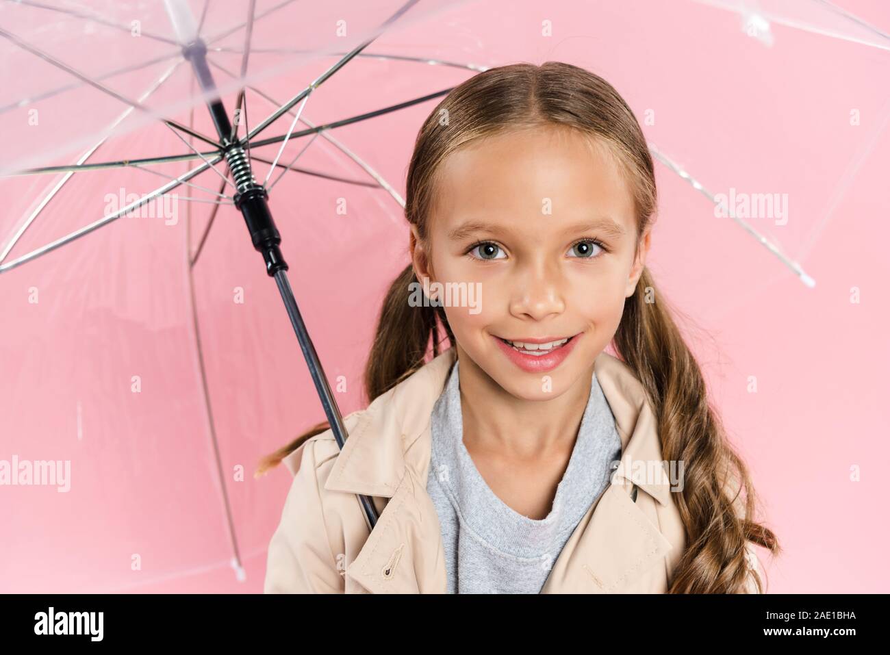 high angle view of smiling kid in autumn outfit holding umbrella isolated on pink Stock Photo