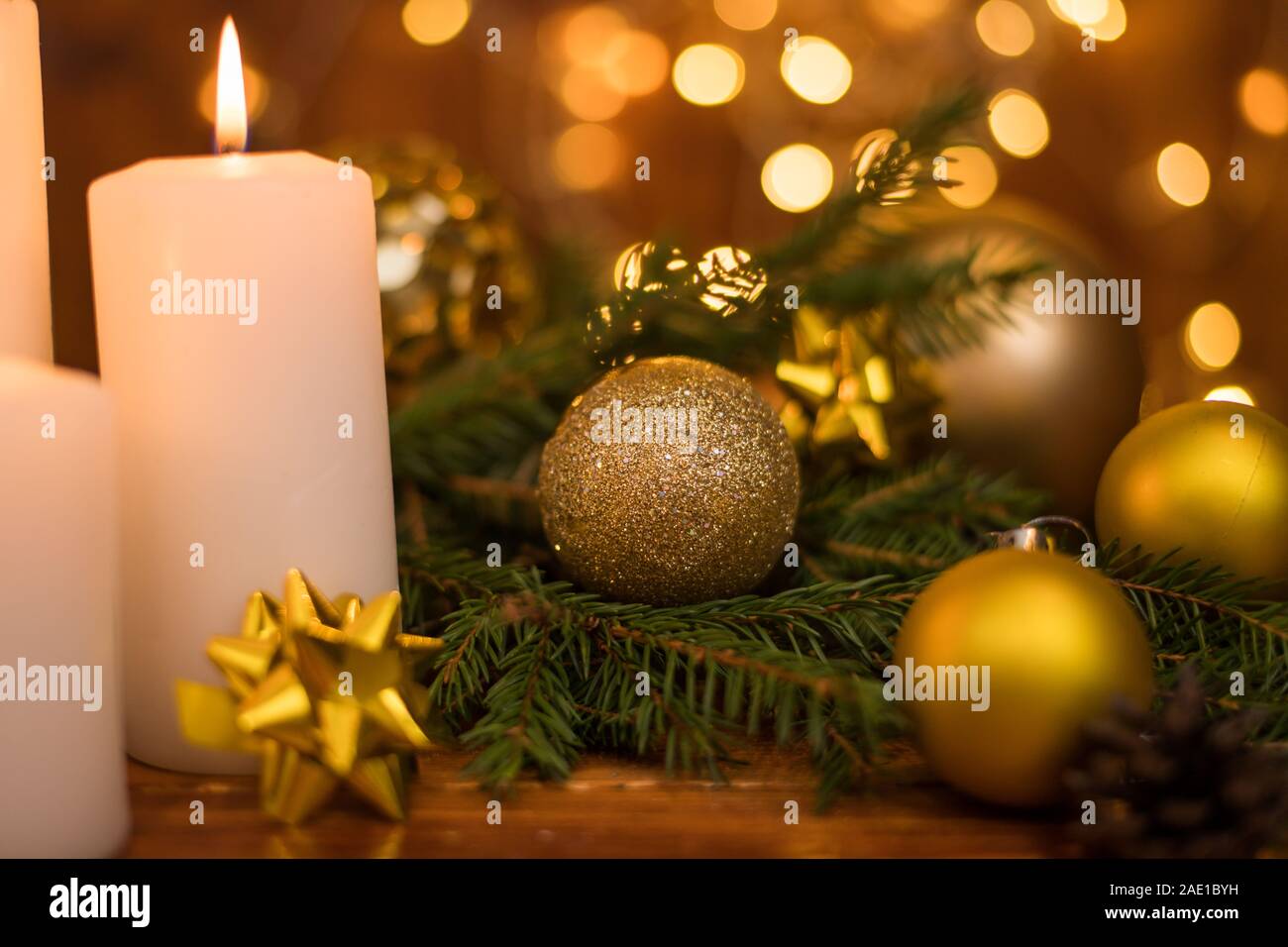 Golden Christmas ball on a tree branch, white candle flame, bokeh lights on a background Stock Photo