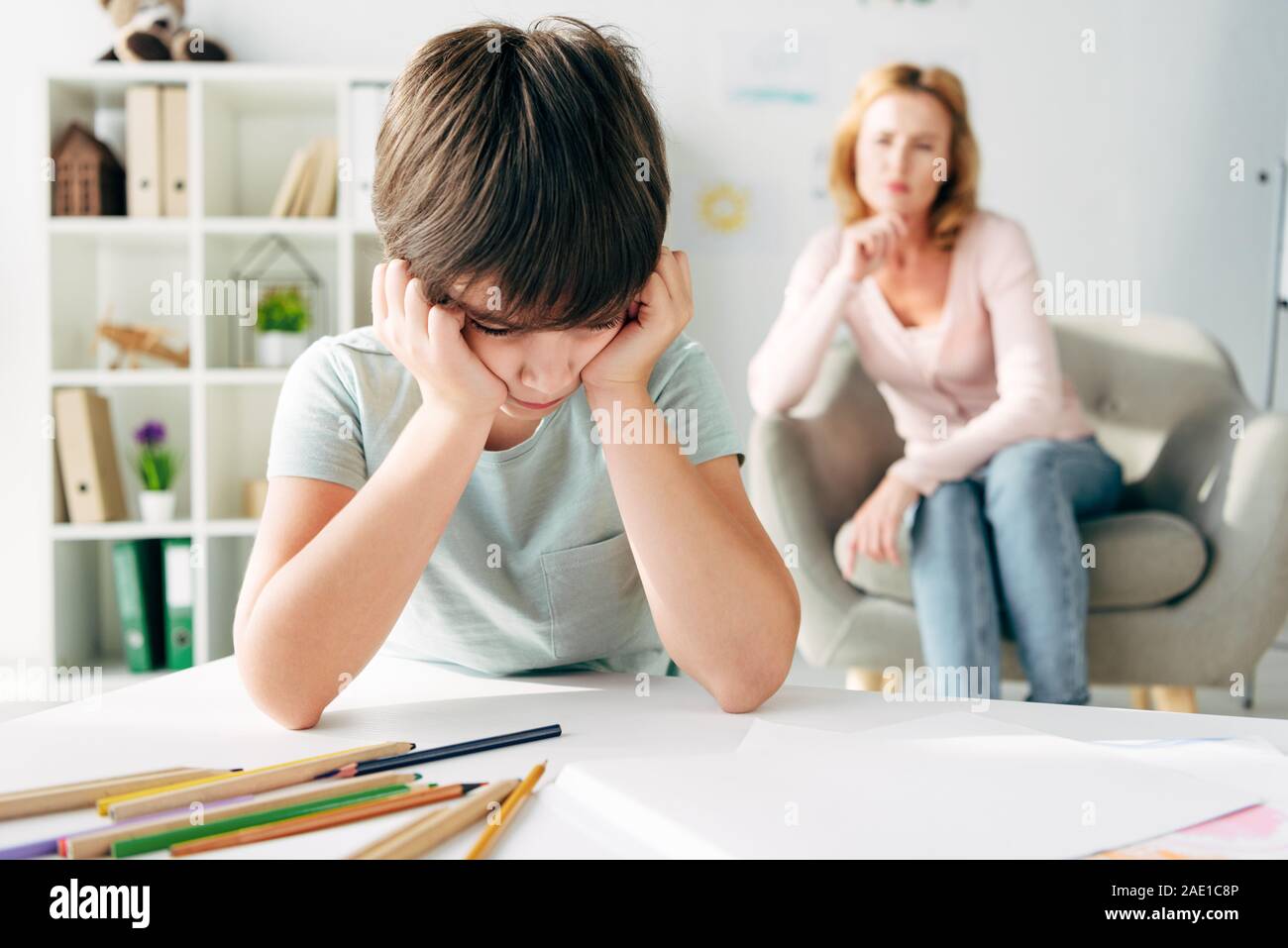 selective focus of sad kid with dyslexia and child psychologist on background Stock Photo