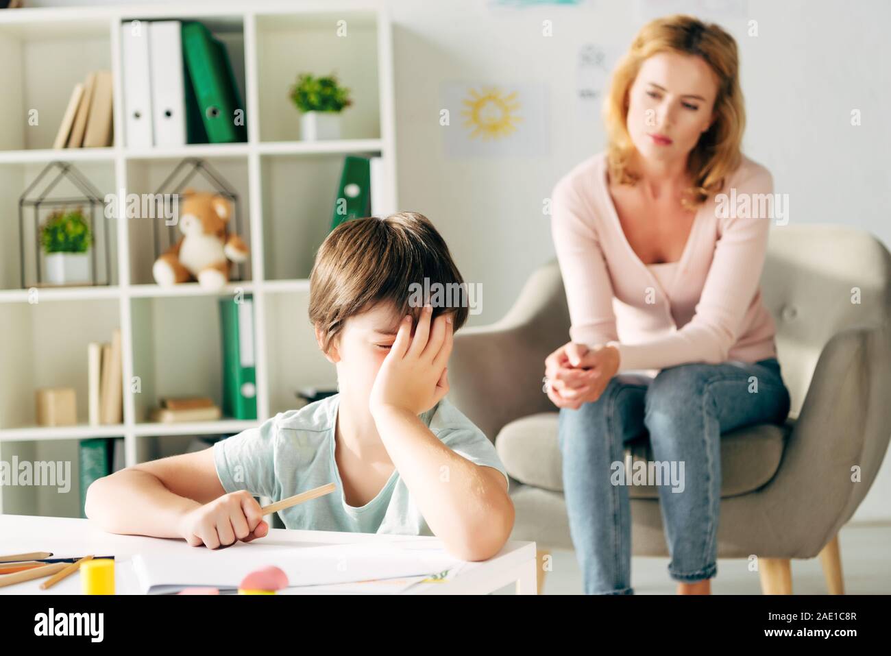 sad kid with dyslexia holding pencil and child psychologist on background Stock Photo