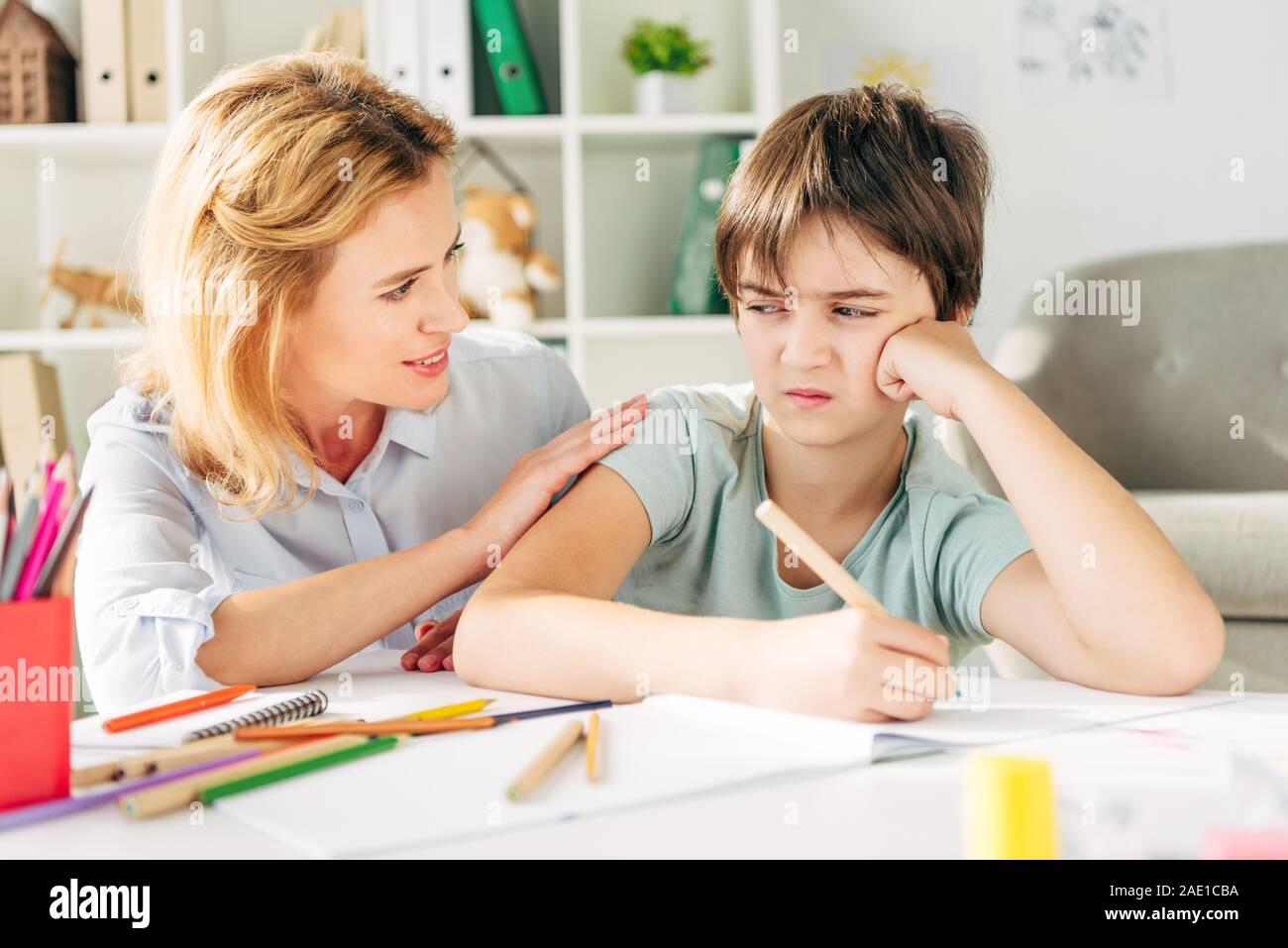 sad kid with dyslexia holding pencil and smiling child psychologist talking to him Stock Photo