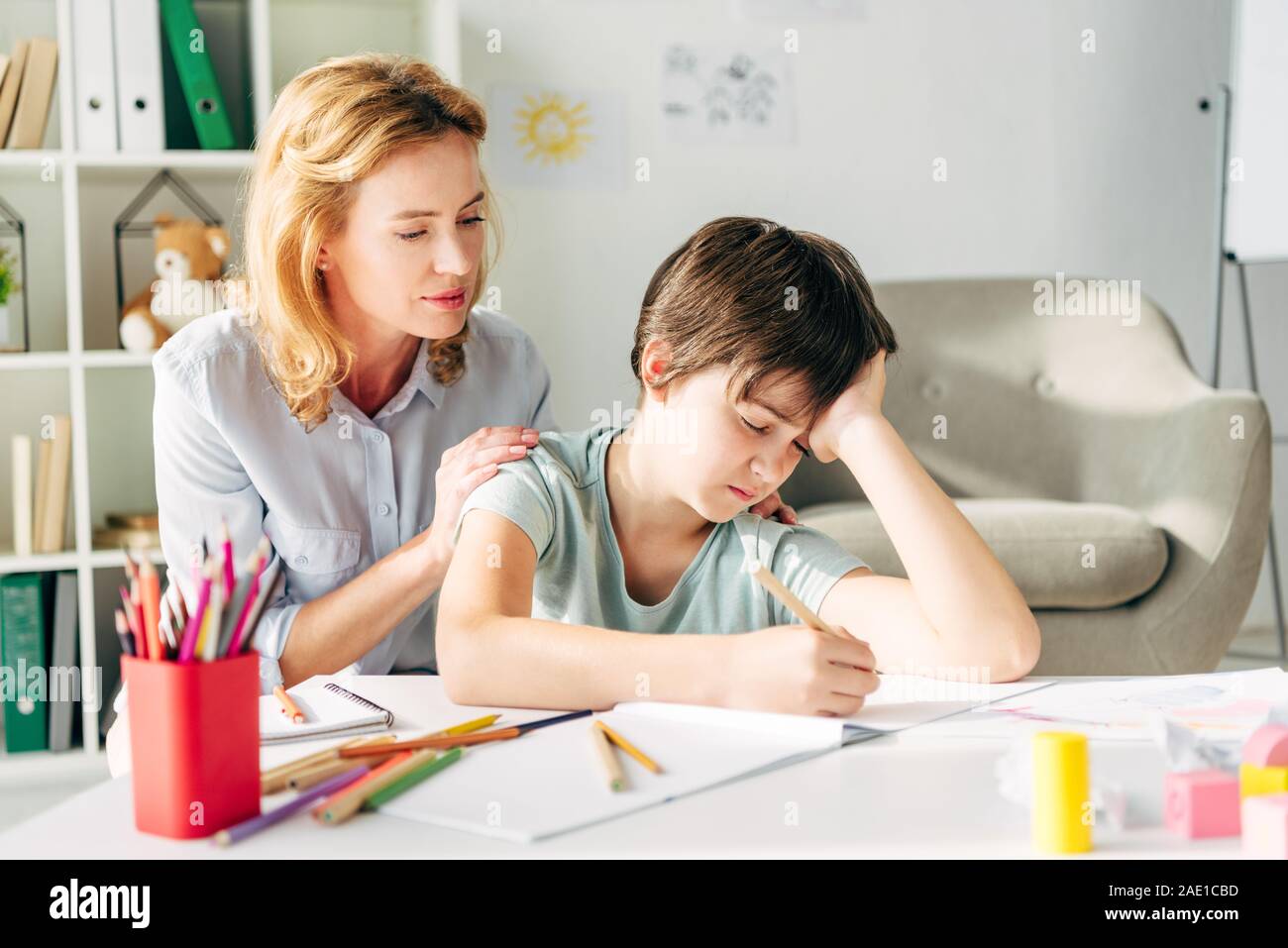 kid with dyslexia drawing with pencil and child psychologist looking at
