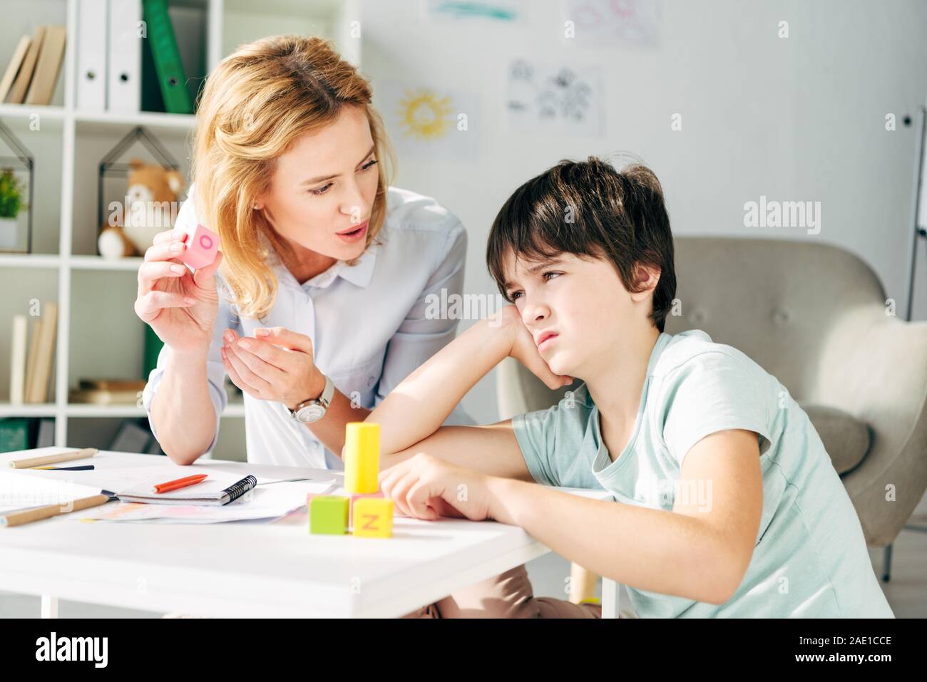 sad kid with dyslexia and child psychologist playing with building
