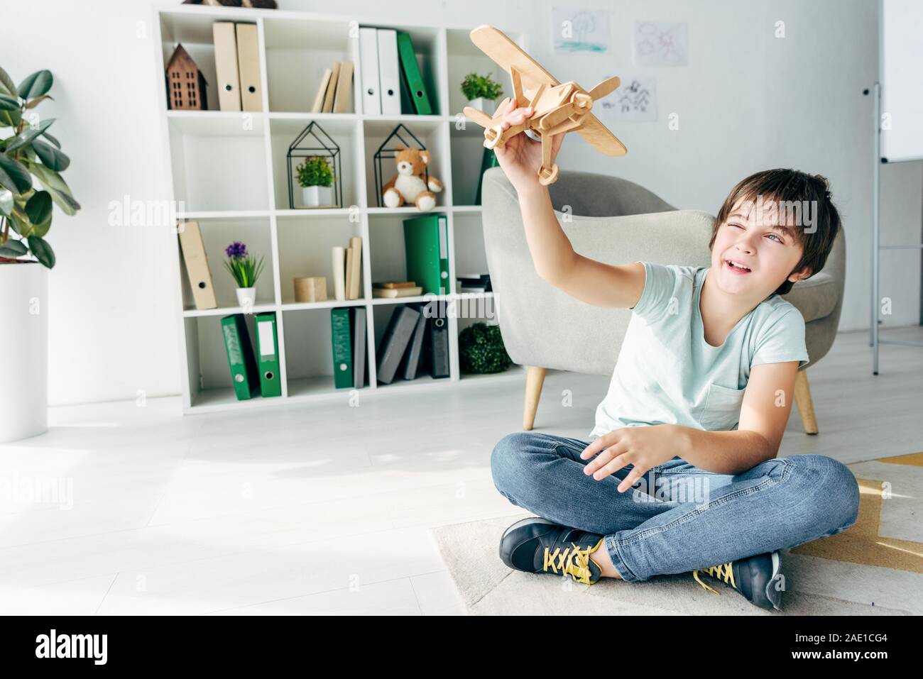 cute kid with dyslexia sitting on floor and playing with wooden plane ...