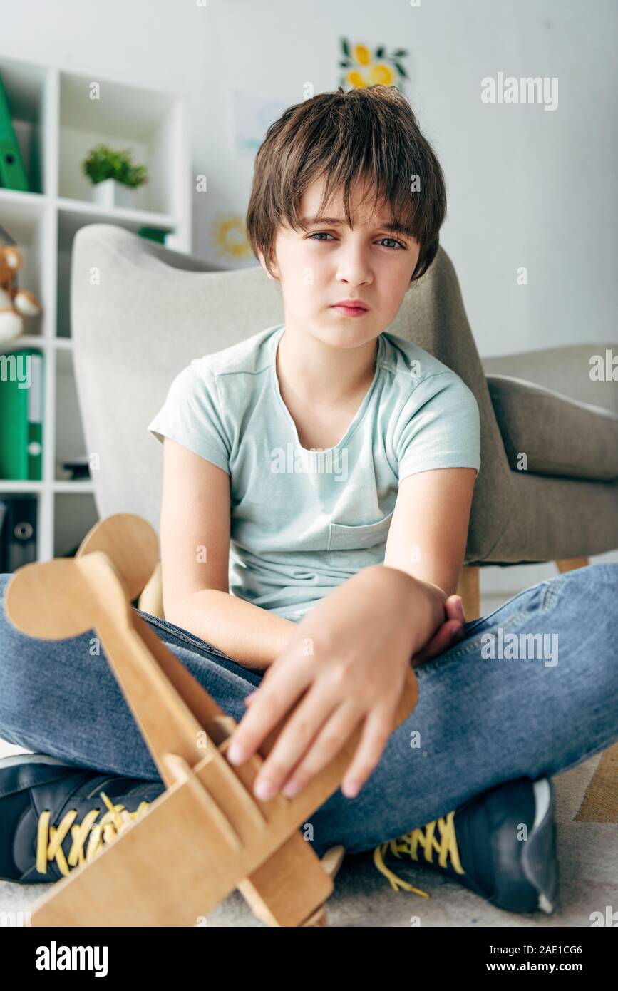 sad kid with dyslexia sitting on floor and holding wooden plane Stock ...