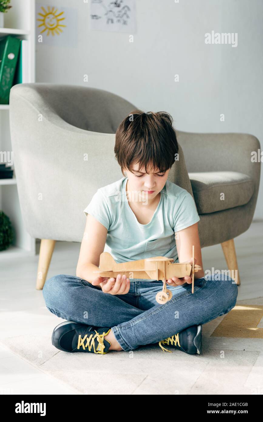 sad kid with dyslexia sitting on floor and holding wooden plane Stock ...