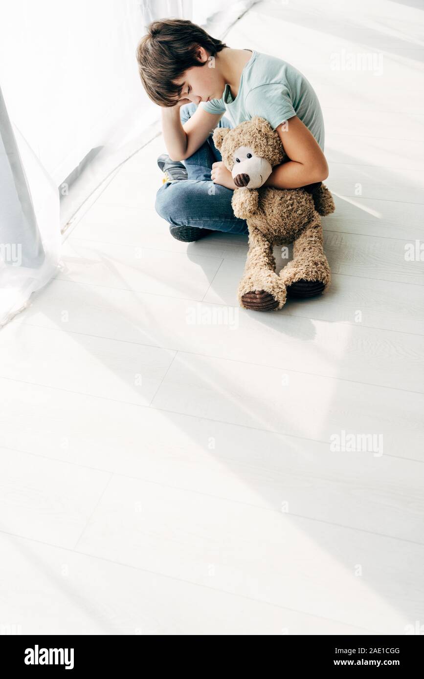 high angle view of kid with dyslexia sitting on floor with teddy bear ...