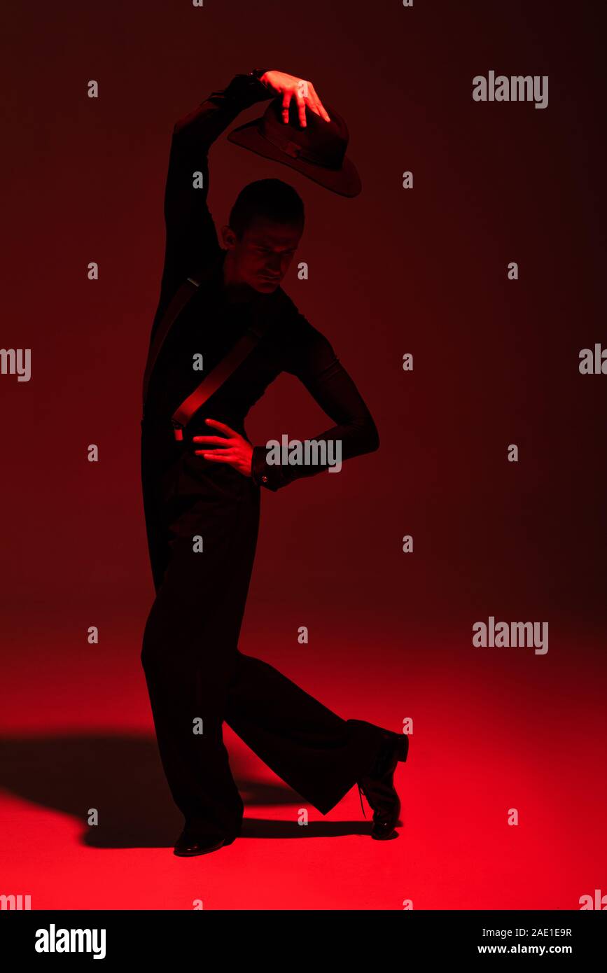 elegant dancer holding hat above head while performing tango on dark