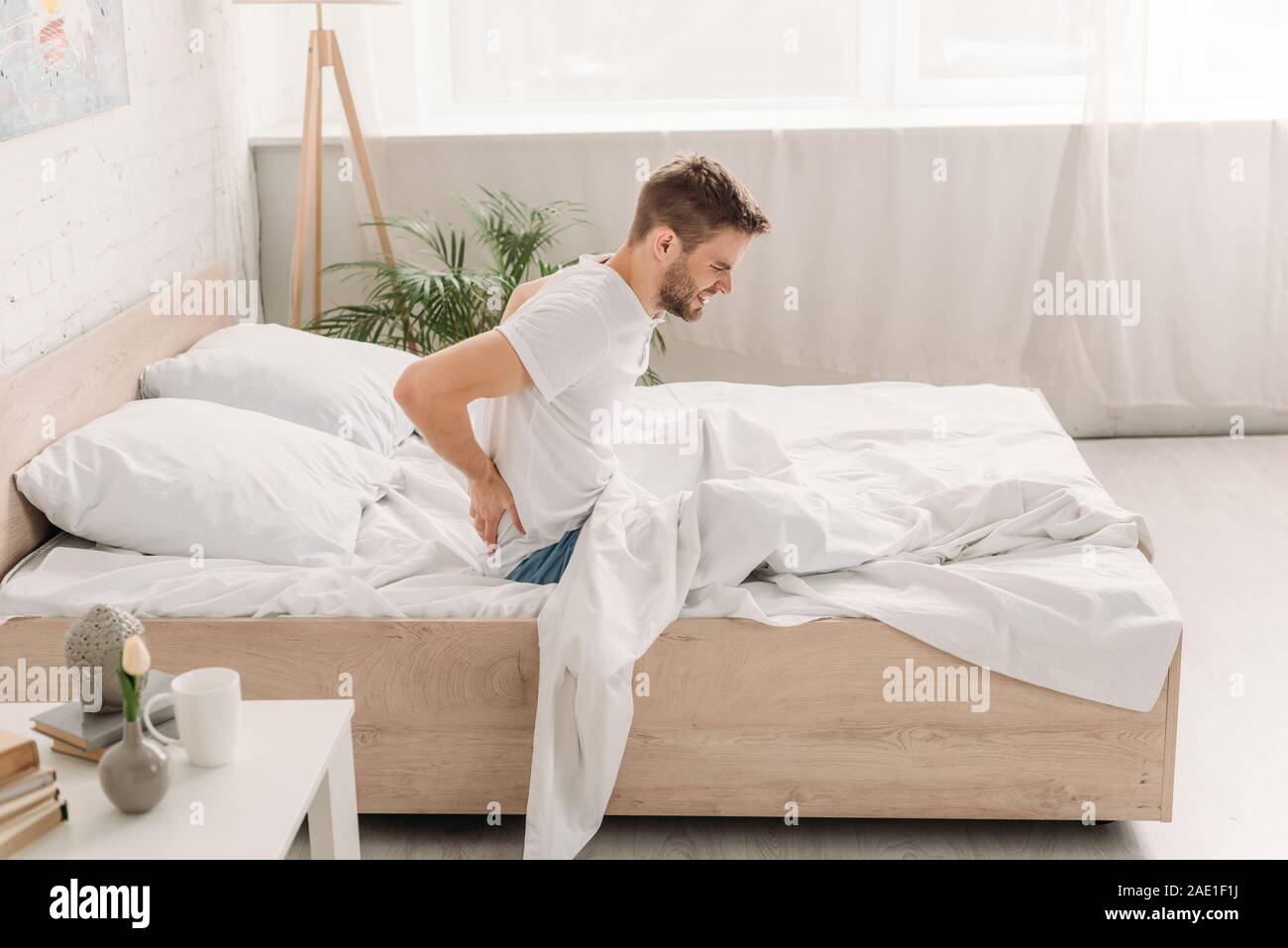 young man sitting in bed and suffering from pain in back Stock Photo ...