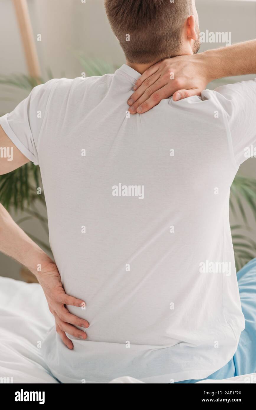 back view of man sitting on bed and suffering from back pain Stock Photo