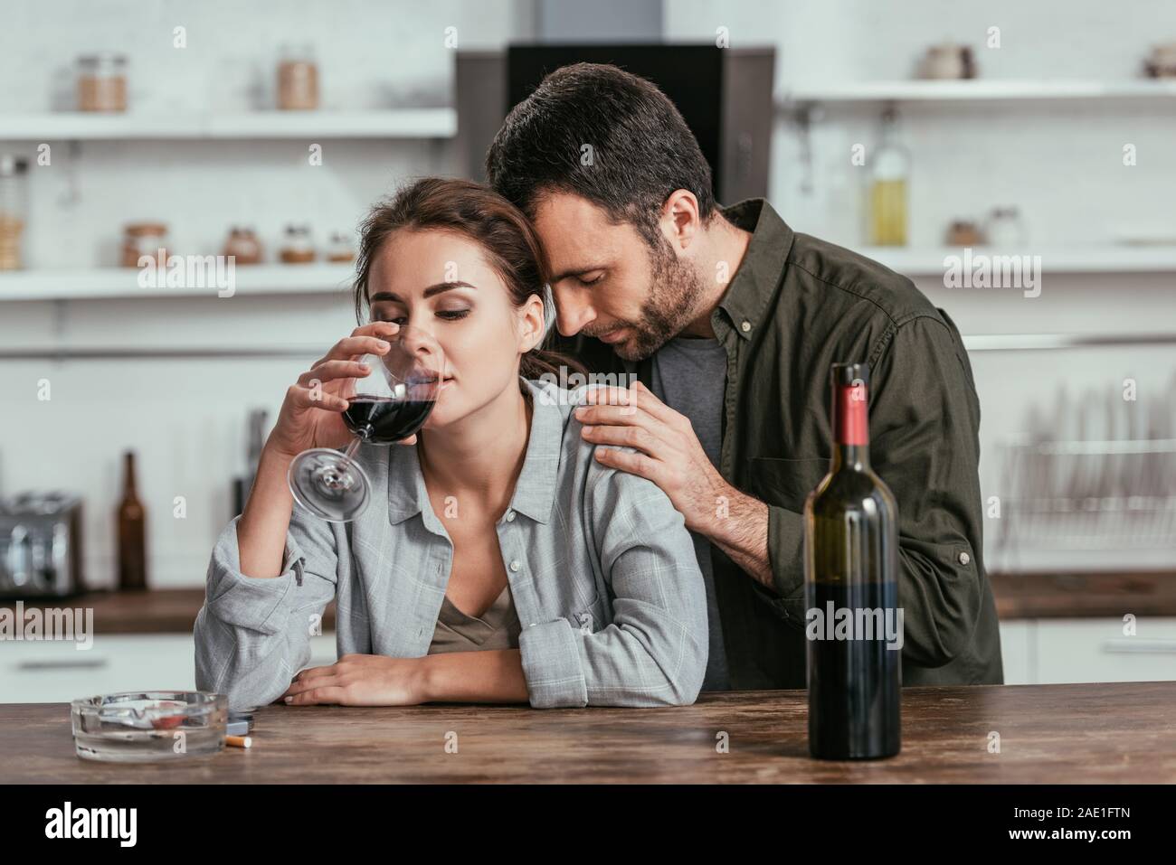 Upset man hugging alcohol addicted wife with wine glass at kitchen ...