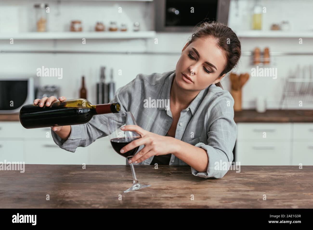 Upset woman pouring wine in glass at kitchen table Stock Photo