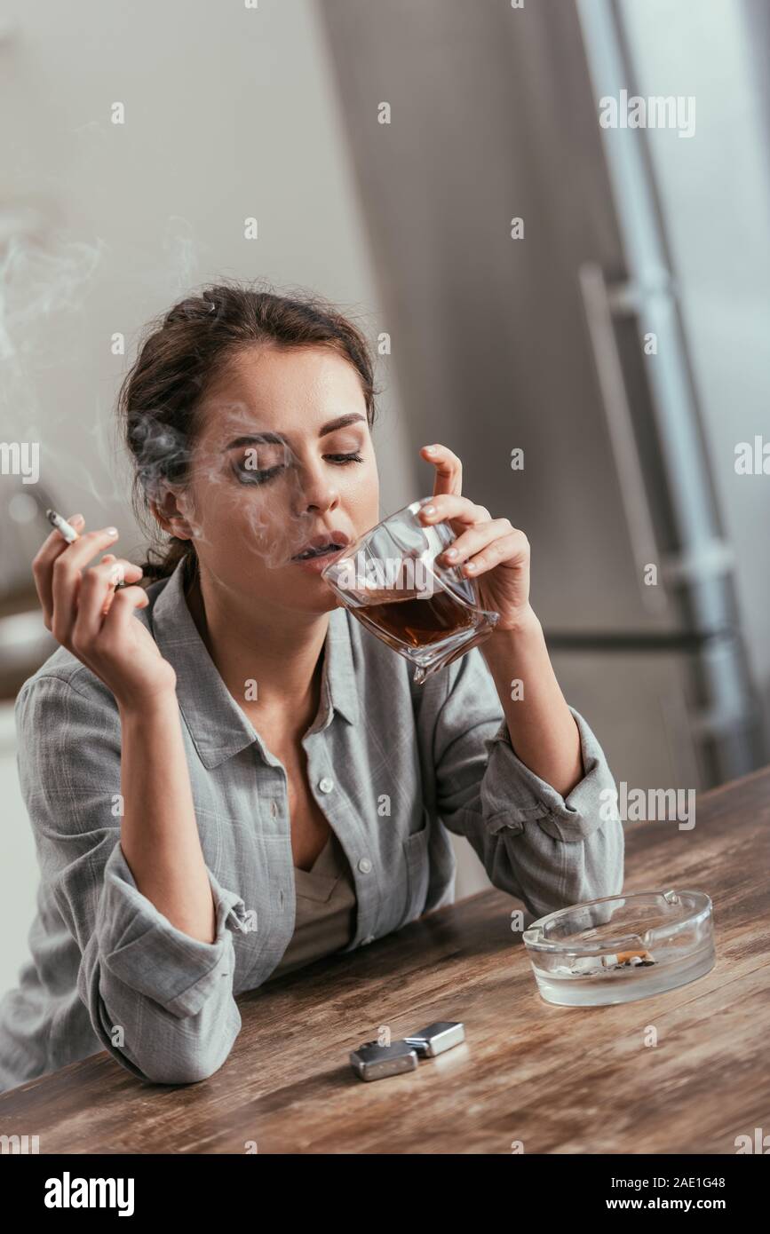 Woman smoking cigarette and holding whiskey glass at table Stock Photo
